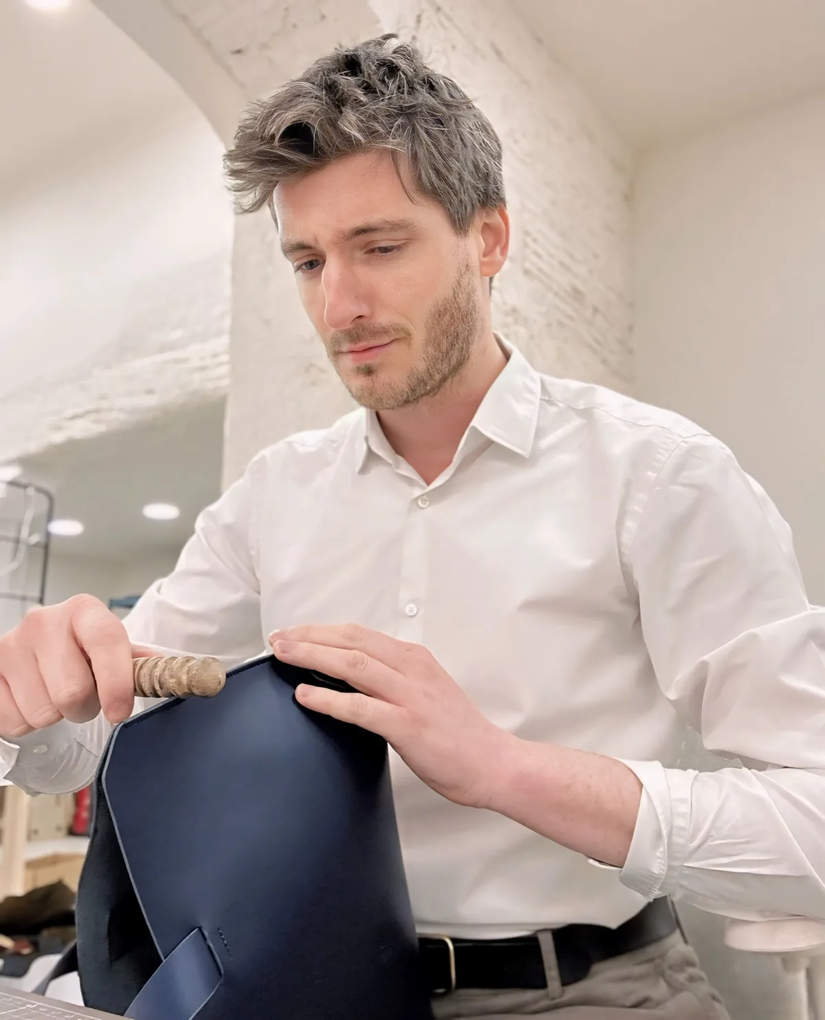 Manuel Dreesmann rematando a mano una pieza de piel azul en el banco de trabajo del taller