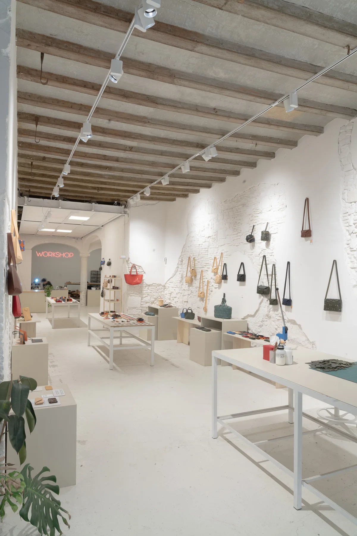 Vista completa del local de Atelier Madre con los bolsos colgados del muro de piedra y las piezas pequeñas sobre las mesas centrales